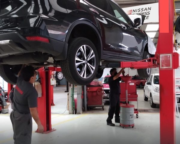 Vista lateral 3/4 de Nissan en rampa de servicio con asesores especializados en servicio brindando mantenimiento.