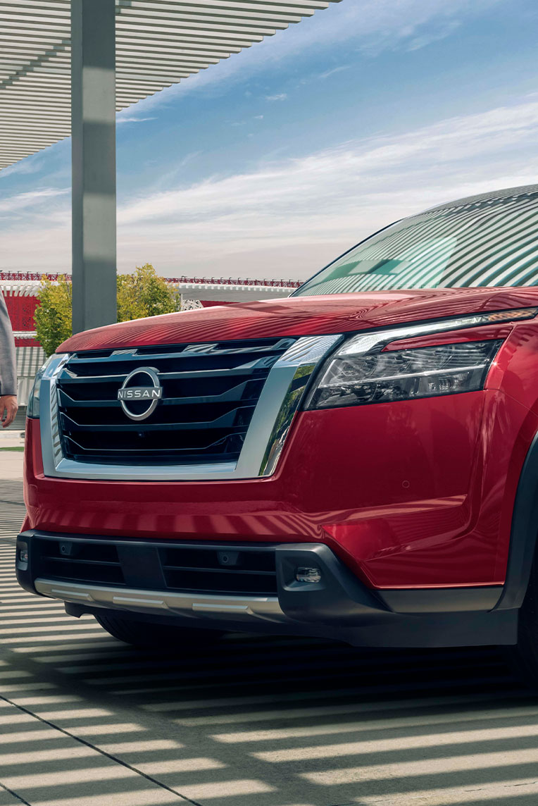 Un hombre con traje gris se acerca al frente del Nissan Pathfinder podemos ver su nuevo diseño exterior