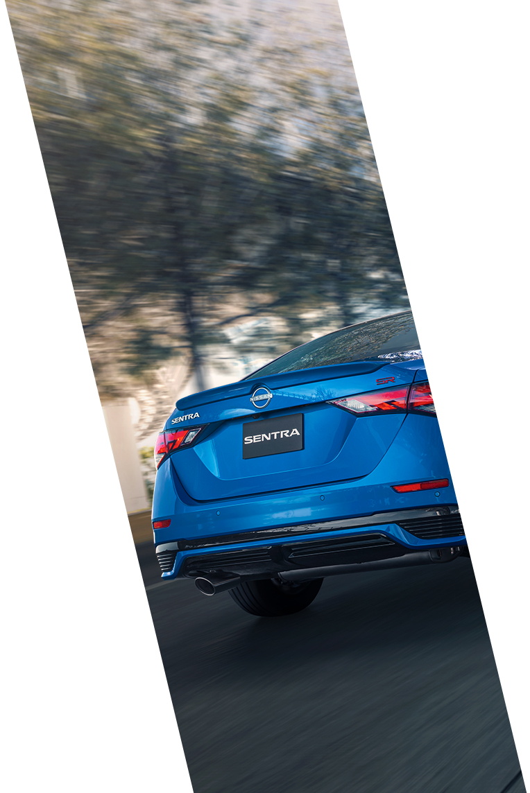 Vista trasera del Nissan Sentra 2024 color azul, destacando sus líneas elegantes, luces traseras y escape mientras se desplaza a alta velocidad en carretera.