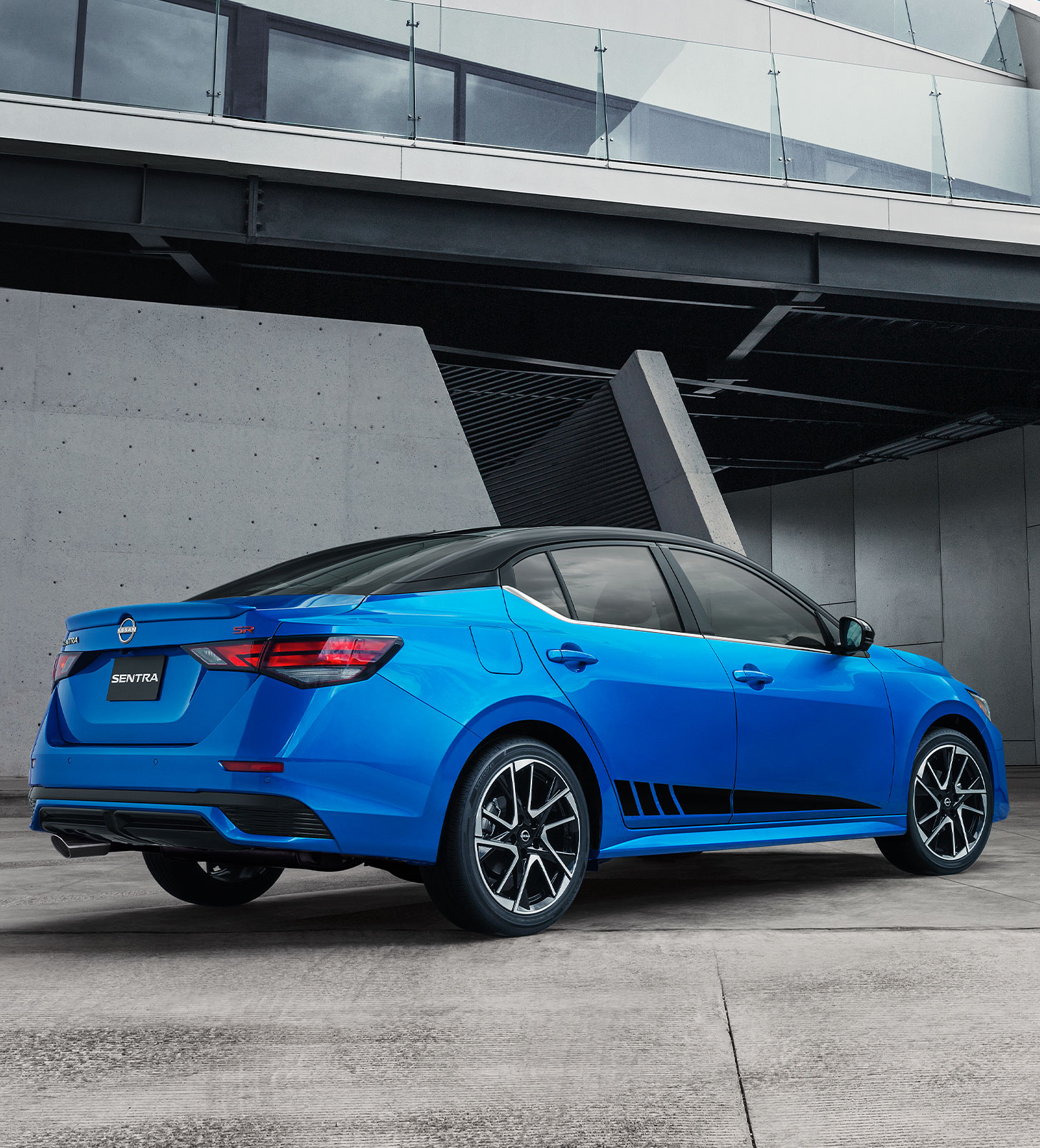 El Nissan Sentra 2024 en azul resplandece bajo una estructura moderna, reflejando la confianza que brindan sus planes de mantenimiento prepagados.