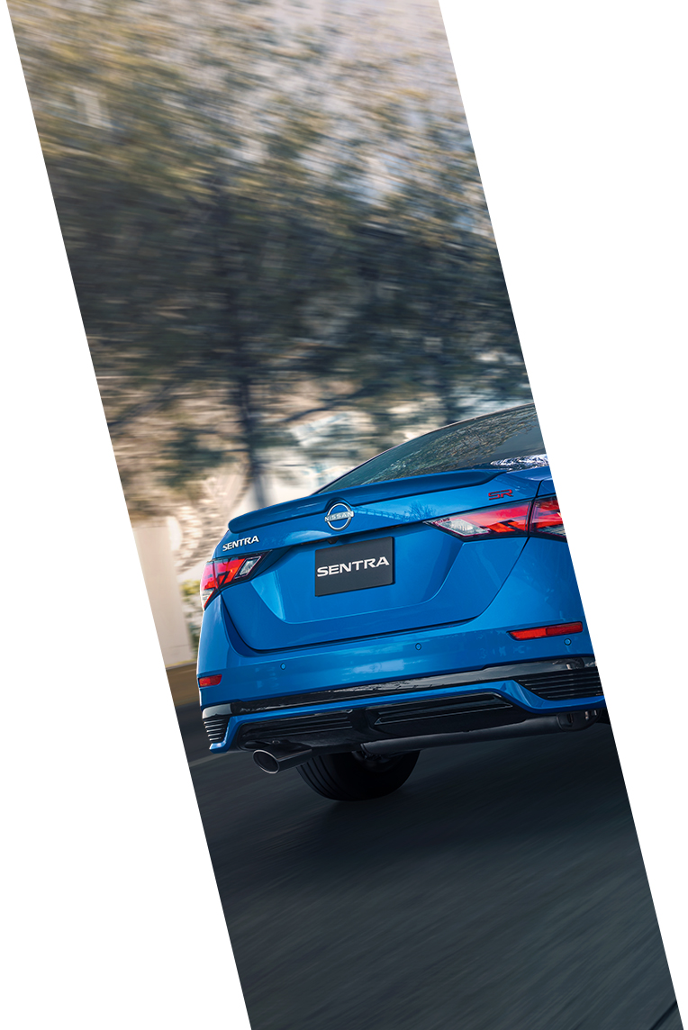 Vista trasera del Nissan Sentra 2025 color azul, destacando sus líneas elegantes, luces traseras y escape mientras se desplaza a alta velocidad en carretera.
