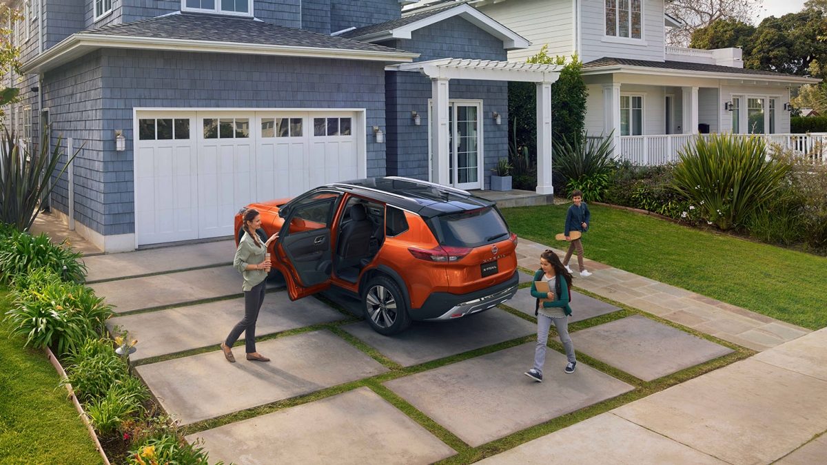 Vista aérea lateral tres cuartos en formato vertical de Nissan X-Trail con familia frente a casa.
