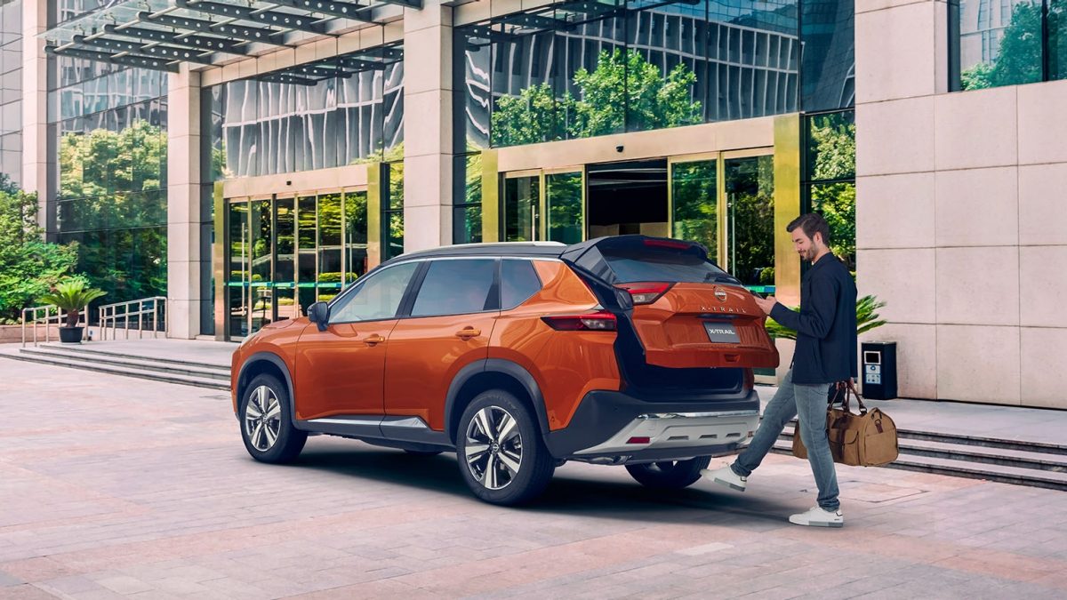 Vista trasera tres cuartos de Nissan X-Trail con hombre abriendo cajuela con sistema de apertura no touch.