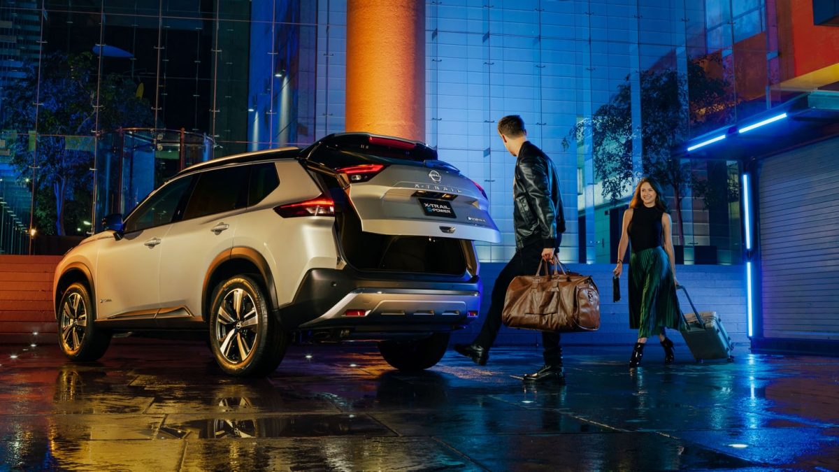Vista trasera tres cuartos de Nissan X-Trail e-POWER con pareja abriendo cajuela con sistema de apertura no touch con amplio espacio de almacenamiento.