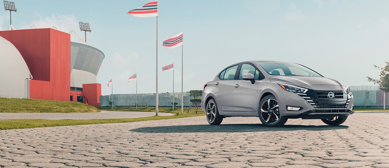 Un hombre camina frente a un Nissan Versa de generación anterior mientras lo mira en un parque citadino