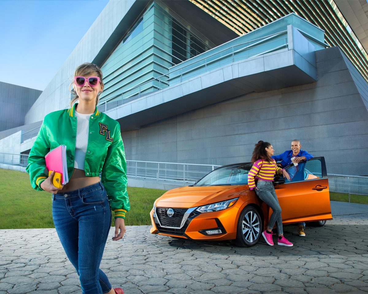 Mujer joven con actitud se aleja de un Nissa Sentra mientras un hombre y una mujer posan junto al auto