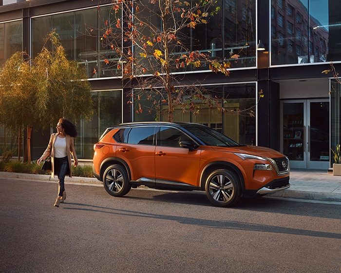 Una mujer con mucha actitud y estilo, cruza una calle mientras vemos una Nissan X-Trail estacionada al fondo