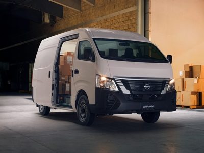Un trabajador de una empresa de reparto se acerca a dos Nissan Urvan blancas junto al río