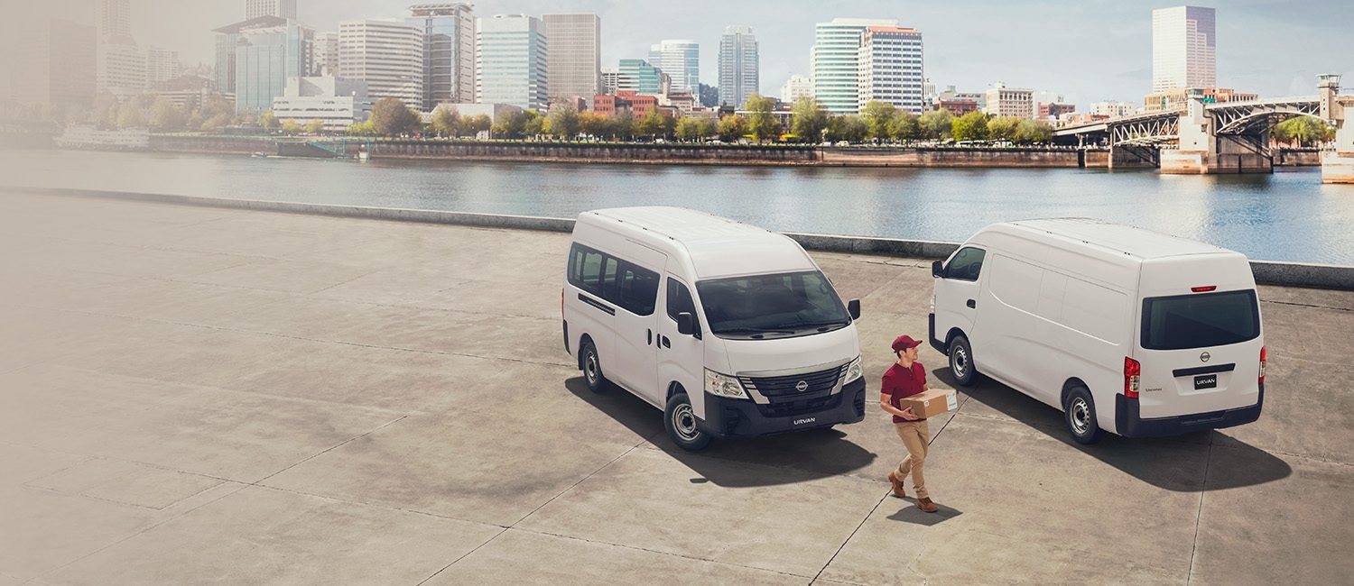 Un trabajador de una empresa de reparto se acerca a dos Nissan Urvan blancas junto al río​